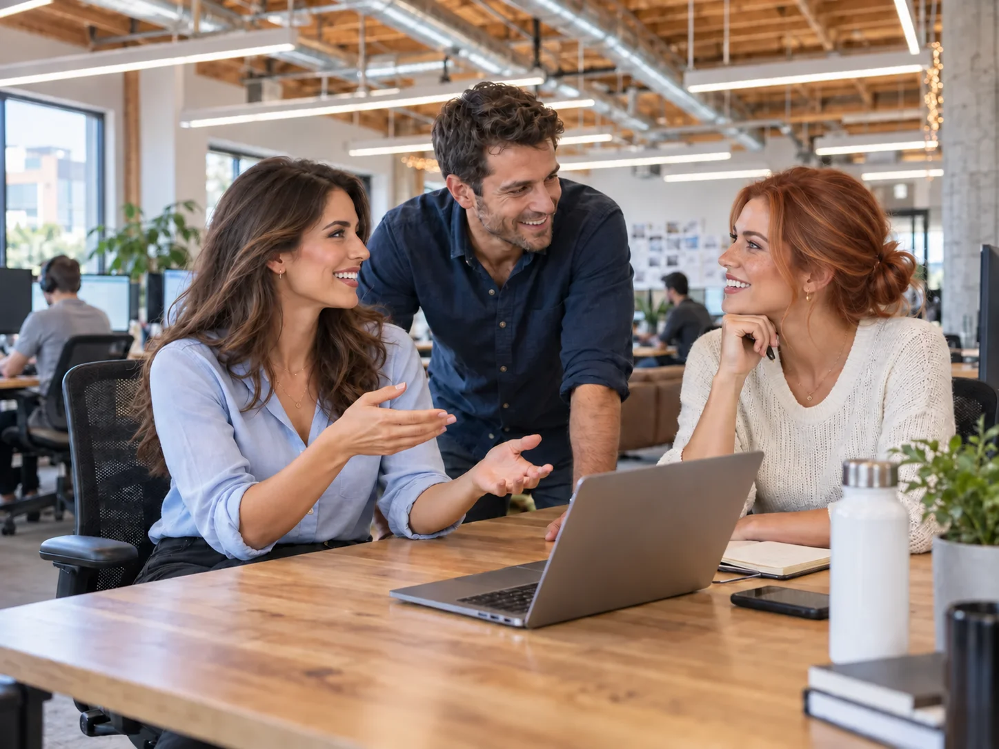 Three coworkers chatting around a laptop in a bright shared office